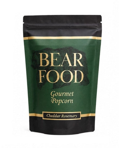 A stand-up pouch of Bear Food Gourmet Popcorn, Cheddar Rosemary flavor, featuring a dark green and black design with gold lettering and borders on a white background.