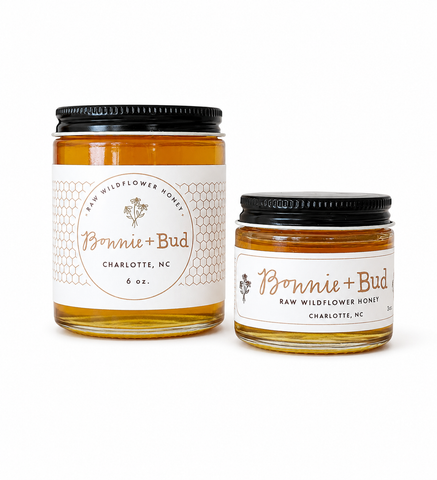 Two glass jars of Bonnie + Bud Raw Wildflower Honey on a white background, one larger 6 oz jar and one smaller jar.