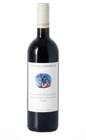 A bottle of Chiara Condello red wine, featuring a dark glass bottle with a white label and a cream-colored foil capsule at the neck. The label displays the brand name 'CHIARA CONDELLO' and a central illustration of a woman in a blue and purple dress.