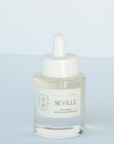 A clear glass bottle with a white dropper labeled 'Seville'. The liquid inside is clear, likely a skincare product.