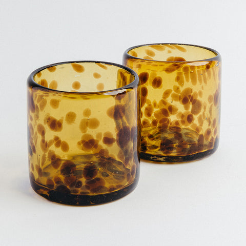 Two amber-colored glass tumblers with a spotted pattern on a white background