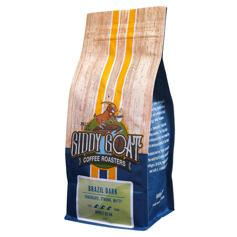 A bag of The Sippy Goat Coffee Roasters Brazil Dark whole bean coffee, featuring a wood-grain patterned top half with yellow stripes, a blue lower half, and a green label at the bottom.