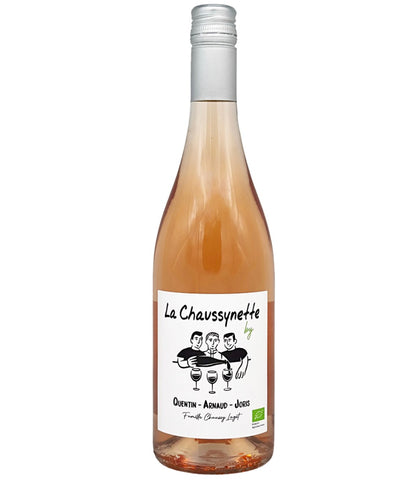 A bottle of La Chavssynette organic rosé wine with rose gold liquid, a white label with black cartoon illustration, and a silver screw cap, shown on a white background.