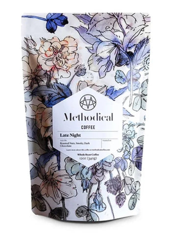 A stand-up pouch of Methodical Coffee 'Late Night' whole bean coffee, featuring a white background with a blue and purple floral pattern and a central white label.
