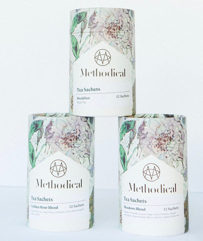 Three cylindrical Methodical tea sachet tins stacked in a pyramid arrangement on a white background. The tins feature a white label with a floral illustration and the brand name 'Methodical' printed in black.