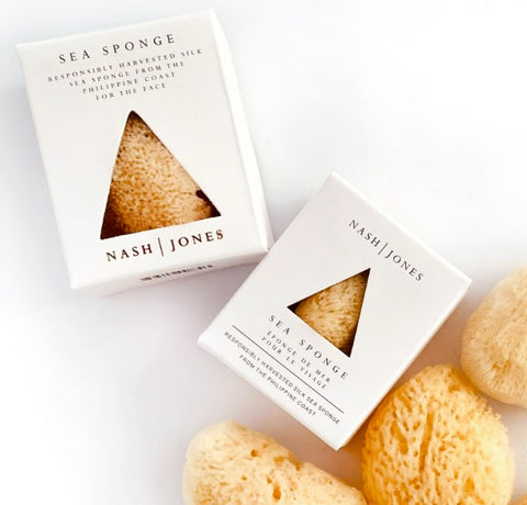 Two white Nash Jones Sea Sponge boxes with triangular cutouts showing the natural sea sponge inside, arranged on a white background with several natural sea sponges around them.