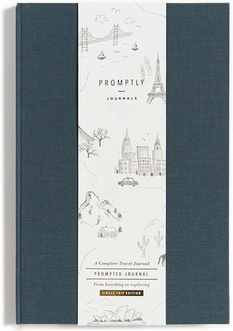 Promptly Journals Single Trip Edition travel journal with a dark slate blue-gray textured cover and a central white paper sleeve featuring black line drawings of landmarks and travel scenes.