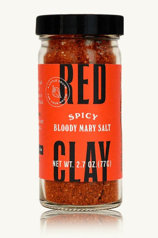 A glass jar of Red Clay Spicy Bloody Mary Salt with a bright orange label and black lid, set against a clean off-white background with a subtle reflection.