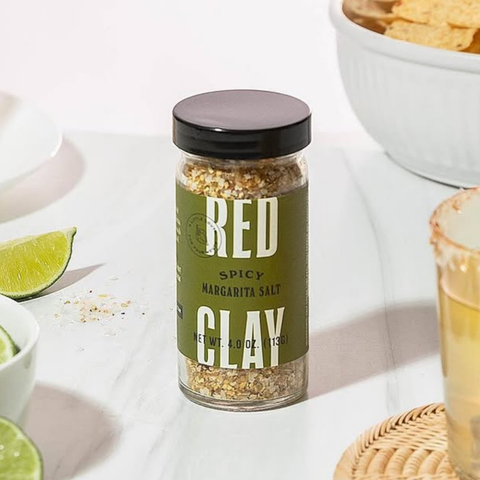 Jar of Red Clay Spicy Margarita Salt on a table with lime wedges and a margarita.