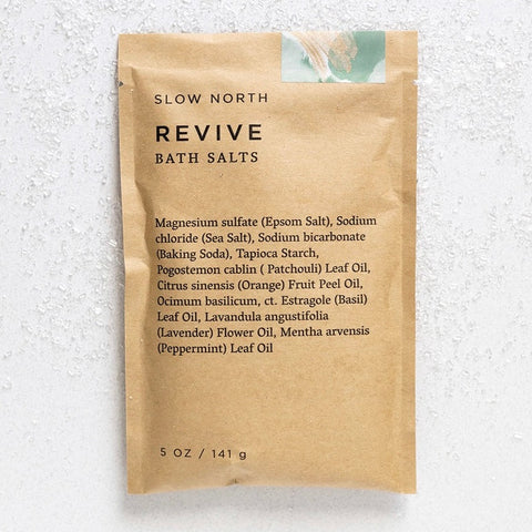 A single brown kraft paper pouch of Slow North Revive Bath Salts, displayed flat against a textured white background.