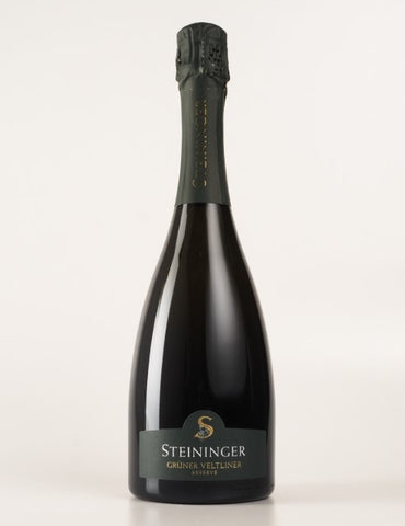 Steininger Crüte Veltliner sparkling wine bottle, featuring a dark glass body, a black foil capsule, and a dark green label with gold lettering, set against a plain light background.