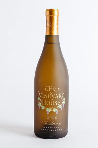 A bottle of The Vineyard House Oakville Chardonnay Napa Valley wine with a white label and gold foil on a white background.