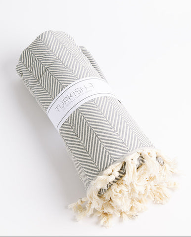 A gray Turkish-T herringbone weave blanket rolled up with a white label on the side, placed on a white background.