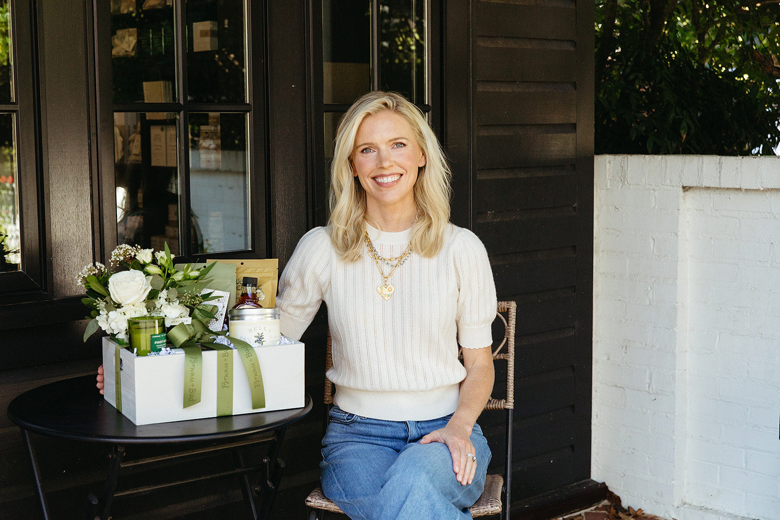 Woman sitting at a table with a gift box and flowers in an outdoor setting