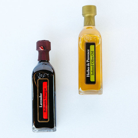 Two bottles of gourmet olive oil and balsamic vinegar placed side by side on a white surface.